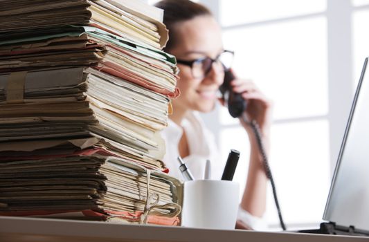 Stack of documents, secretary speaking on the phone in the background