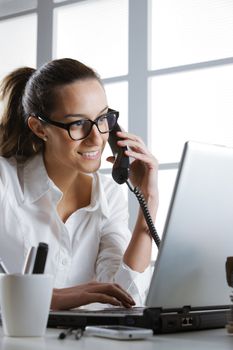 Beautiful young woman working in office and making a phone call