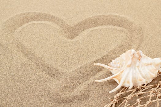 handwritten heart on yellow soft sand with seashell and shallow focus