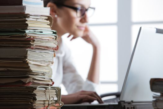 Stack of documents, with secretary who works at the computer in the background