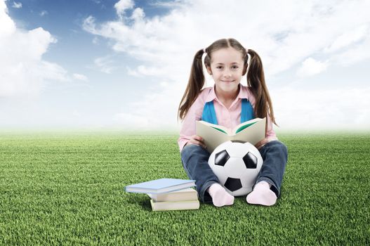 Cute little girl with books and soccer ball on green grass