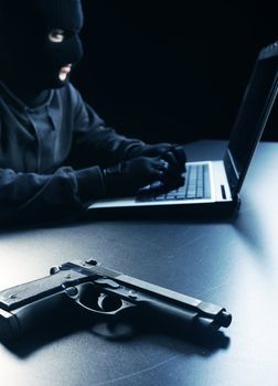 Computer hacker - Male thief stealing data from laptop, focus on gun