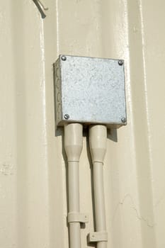 A metal box with screws attached to a metal wall with a pair of cables leading to it.
