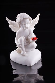 Close up of a little statue of an angel with a red heart on the hand