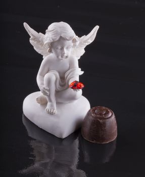 Close up of a little angel and a chocolate over black background