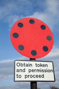 Railway warning symbol in red and black with a rectangular sign with the words 'obtain token and permission to proceed'.
