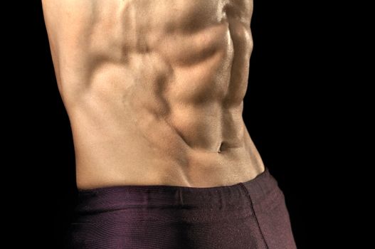 Closeup of shirtless man flexing highly defined abs on black background