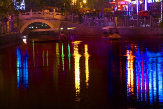 Houhai Lake Bar District Silver Ingot Bridge Red Blue Lights at Night with Reflections Beijing China Trademarks removed.




