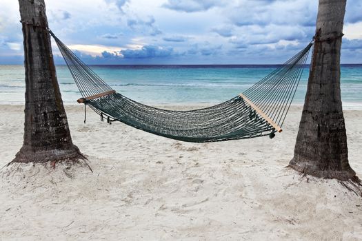 A hammock between two palm trees beside the ocean as the sun begins to set.