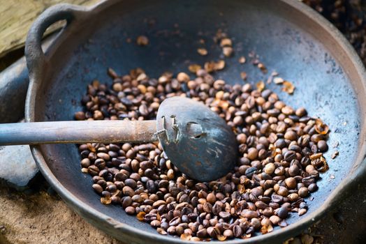 Traditional coffee beans roasting in metal basin with spoon, shallow depth of field
