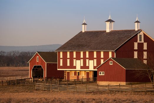 Photograph of am old but well maintained large red barn in facing east towards the morning sun.  Photograph taken in the winter so trees and field are barren or fallow.