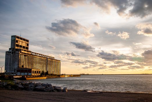Photograph of an abandoned grain elevator near Buffalo New York at sunset with an industrial shore in foreground.