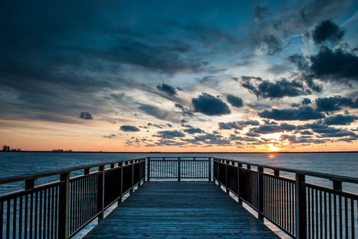 Photograph of a backlit pier near Buffalo New York taken at sunset with multilayered clouds and sun visible.