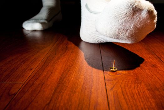 Photograph of a human foot about to step on an upright tack on a wooden floor.