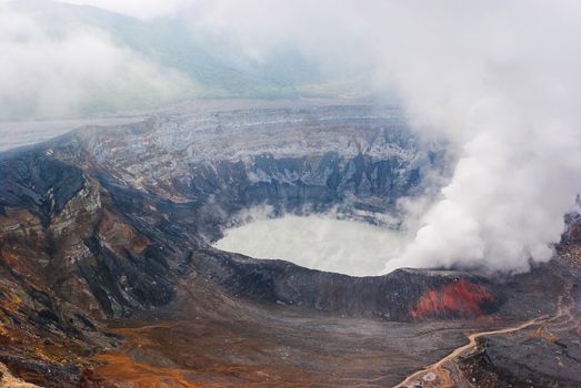 View of the caldera of the Costa Rican volcano known as Poas.  Steam is rising up from the discolored crater and gray lake.