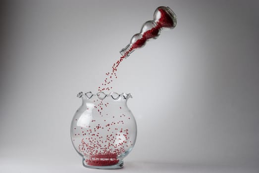 Photograph of a red beads being transferred between one glass vase to another without hands or visible strings.