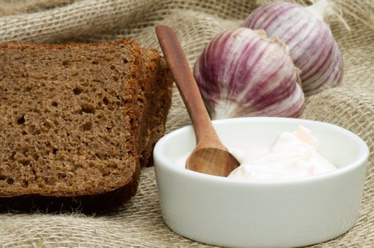 Simple Snack with Sour Cream, Garlic and Brown Bread closeup on Sackcloth background