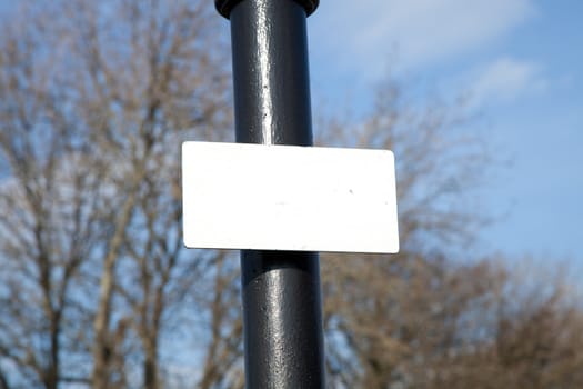 A blank white rectangular sign attached to a black painted post.