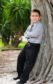 Serious Young boy leaning against tree with arms crossed
