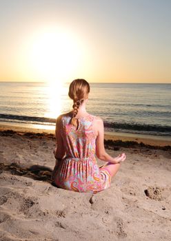 Woman meditating on beach with sunrise