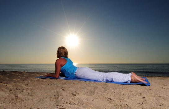 Woman doing sphinx yoga pose on beach during a beautiful sunrise