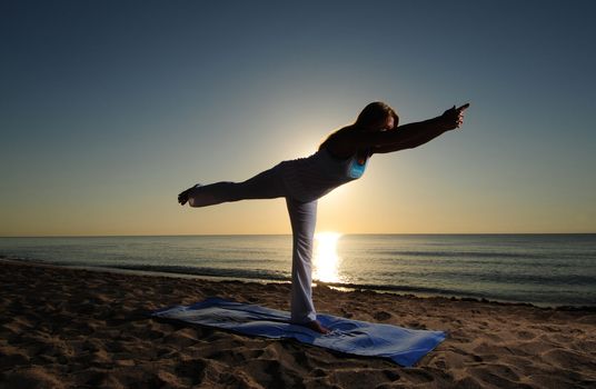 Woman doing yoga Warrior Pose III (Virabhadrasana III) on beach during a beautiful sunrise