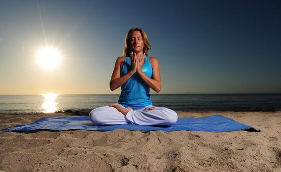 Woman doing Full Lotus Pose for meditation on beach during a beautiful sunrise