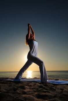 Woman doing Warrior I (Virabhadrasana I) yoga pose on beach during a beautiful sunrise