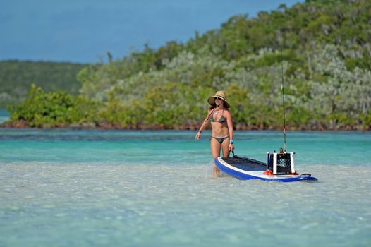 Beautiful woman in bikini pulling paddle board with fishing gear