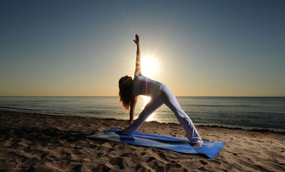 Woman doing Triangle Pose (Trikonasana) yoga  on beach during a beautiful sunrise