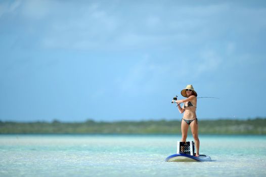 Beautiful woman casting fishing rod while paddleboarding in the Caribbean