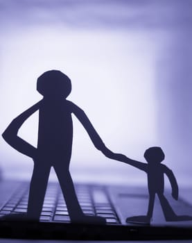 father and son  silhouette cut in small rudimentary figures  in paper , man holding child hand facing a computer

