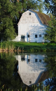 white barn on a farm in the country with a reflection in a pond