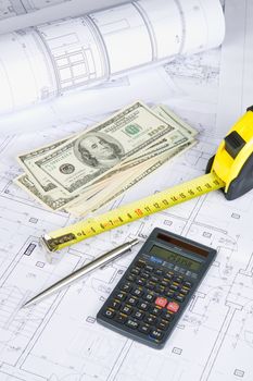 Dollars, measurement tape and calculator on architectural drawing blueprint