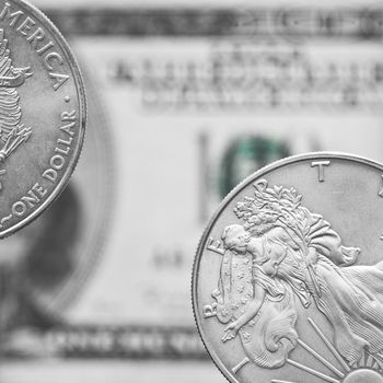 Two silver shiny dollar coins on a background of blurry one hundred dollar bill