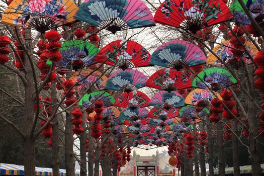 Paper Fans Lucky Red Lanterns Chinese New Year Decorations Stone Gate Ditan Park Beijing China.  During Lunar New Year, many parks and temples in China have large outdoor fairs, festivals.  Chinese characters on lanterns say lucky and long life.