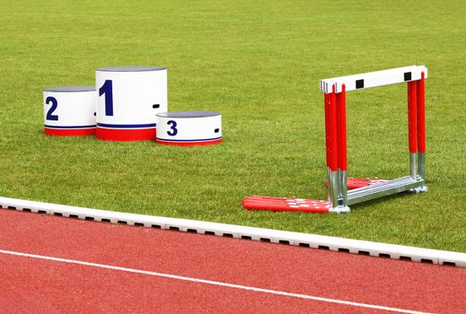 Track lanes with winner's podium and hurdles on green grass