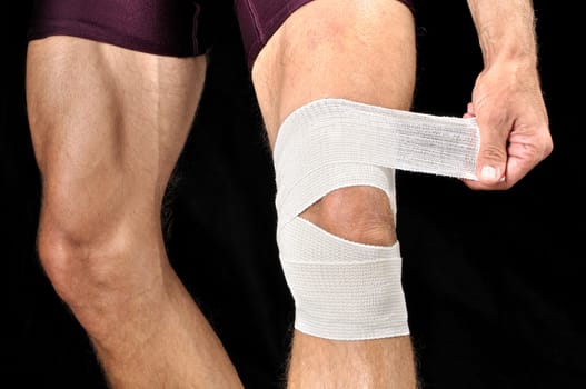 Closeup of man wrapping knee with sports wrap on black background