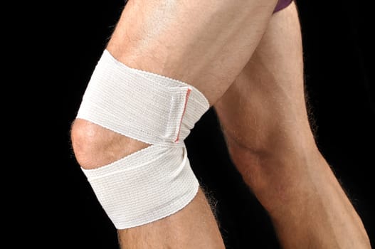 Closeup of man with sports wrap on knee as he runs on black background