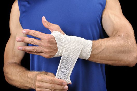 Athletic man in blue shirt wraps his wrist with sports wrap on black background