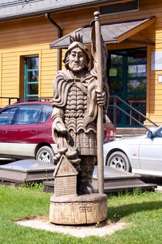 Wooden statue in form of warrior in front of wooden house
