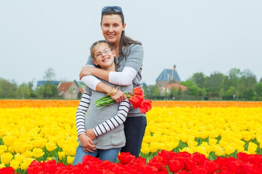 Girl and her mother with bouquet between of the yellow-red tulips field