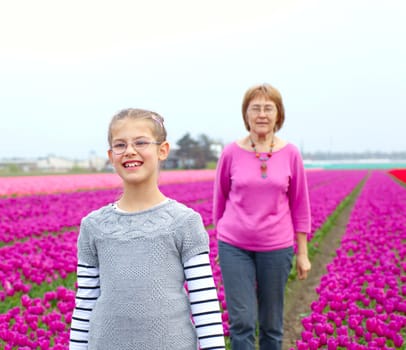 Girl with her grandmother walks between of the purple tulips field