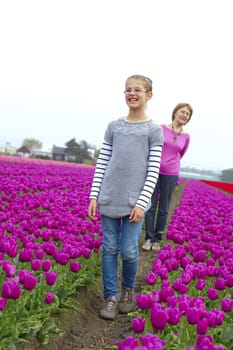 Girl with her grandmother walks between of the purple tulips field
