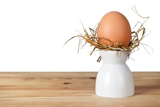 Easter egg in hay nest on white stand. Natural egg. All on old wooden table on white background, isolated
