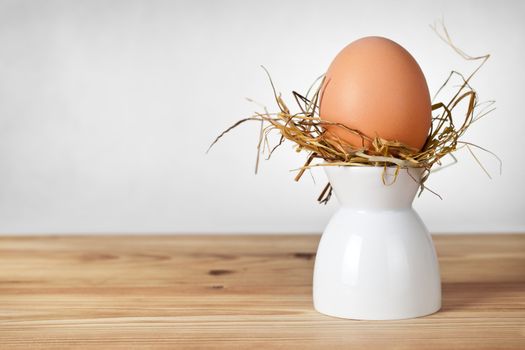 Easter egg in hay nest on white stand. Natural egg. All on old wooden table background
