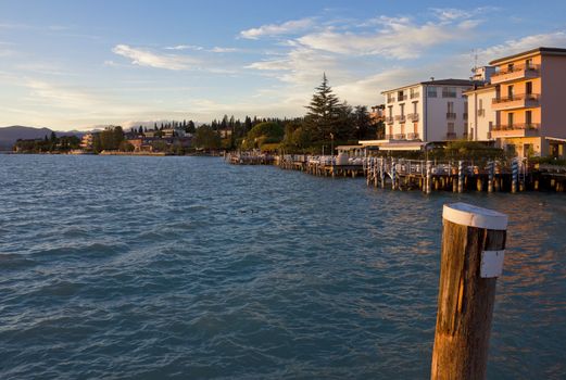 Sunset view of the jetty port and Sirmione waterfront on Lago di Garda, Italy. Warm light over the landscape at lake Garda.