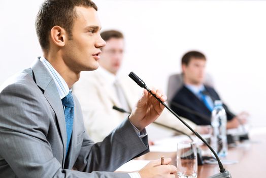 Portrait of a businessman, said into the microphone, in the background colleagues communicate with each other