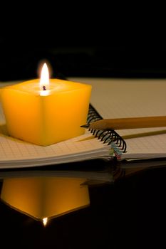 Open notebook pencil and a burning candle in the night