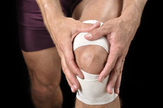 Closeup of athletic man tending wrapped injured knee on black background